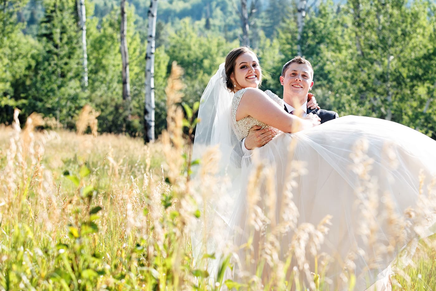 groom carrying bride through a grassy field